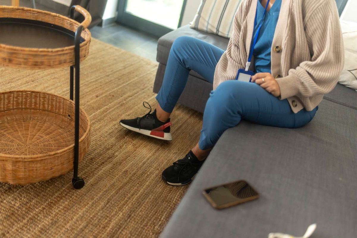 Nurse sitting down after shift in blue scrubs and black runners